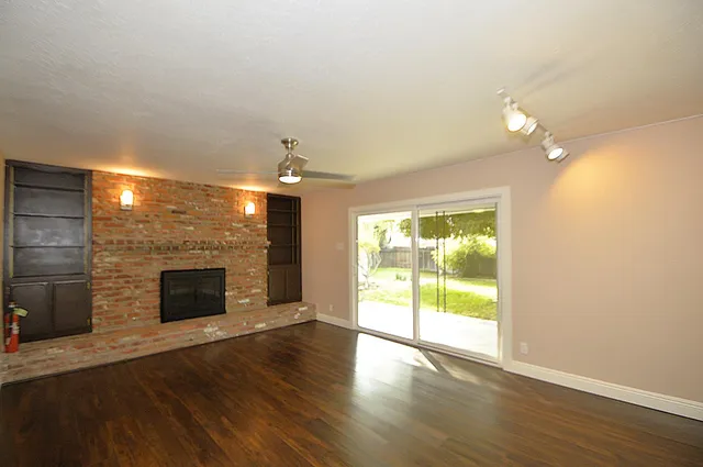an empty room with wooden floor fireplace and windows