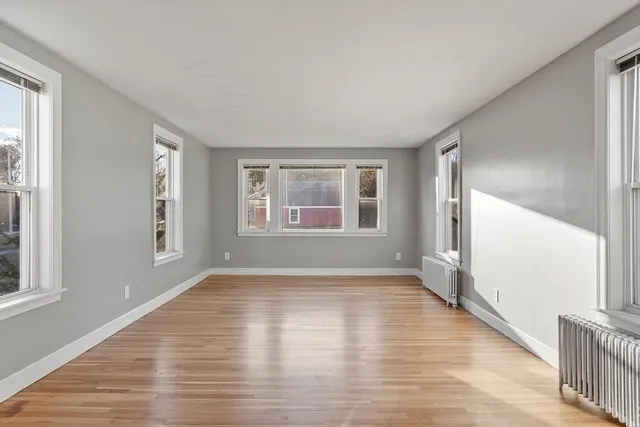 a view of an empty room with wooden floor and a window