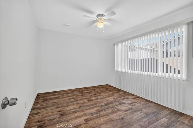 an empty room with wooden floor chandelier fan and windows
