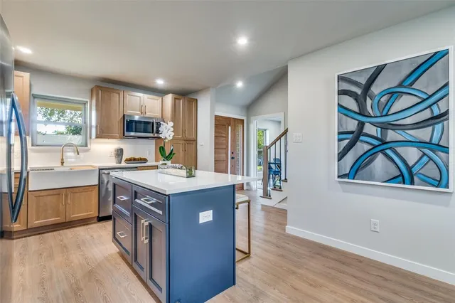 a kitchen with kitchen island granite countertop a stove top oven a sink dishwasher and a refrigerator with wooden floor