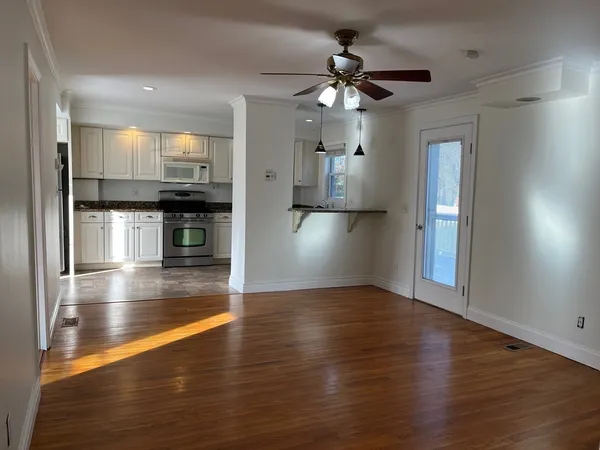 a view of empty room with wooden floor and kitchen