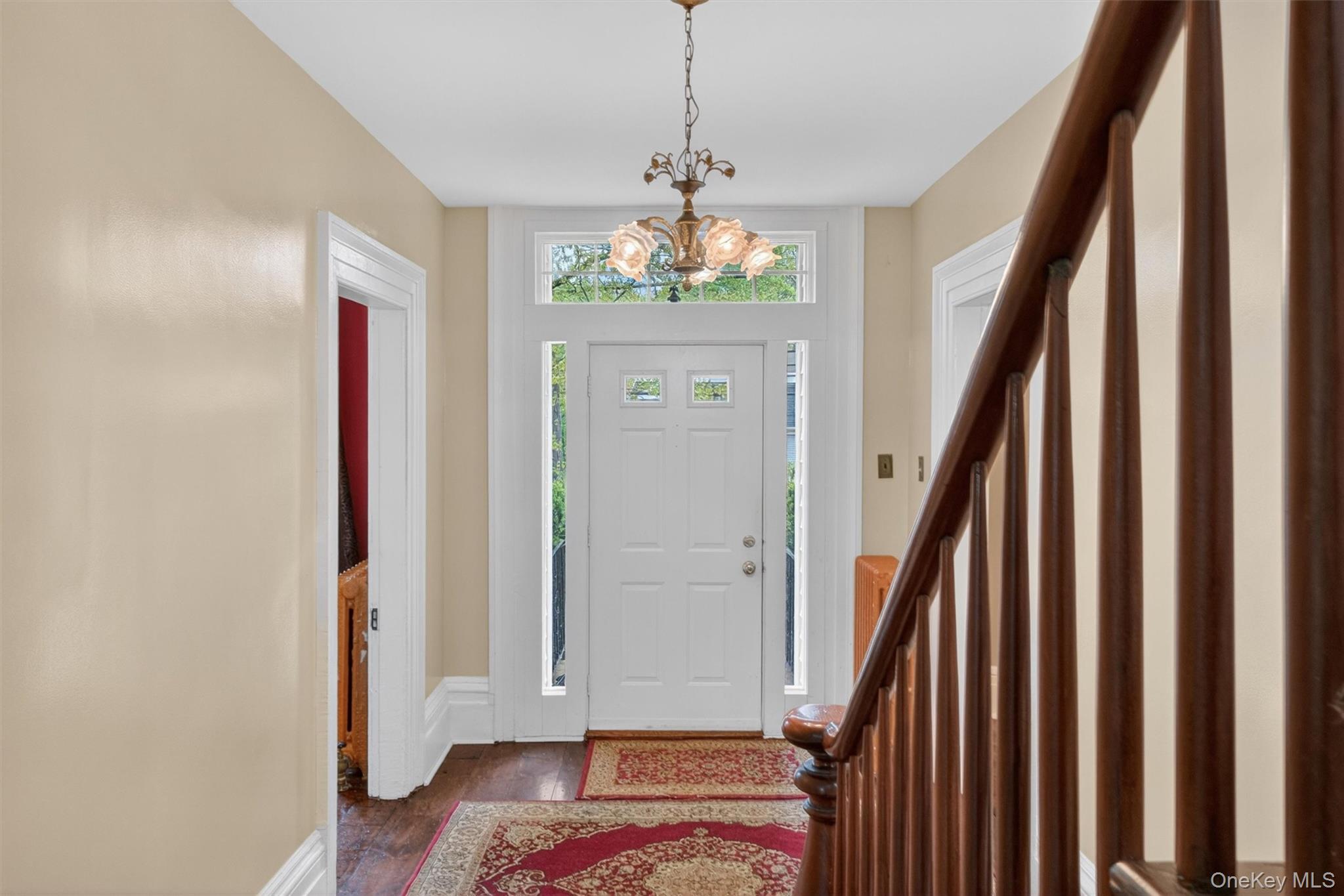 121 Old Glenham Road Fishkill, NY 12524 - Photo 4 of 50 Foyer showcasing a white entry door with a transom window, hardwood flooring, a classic chandelier, and a dark wood staircase with balusters.
