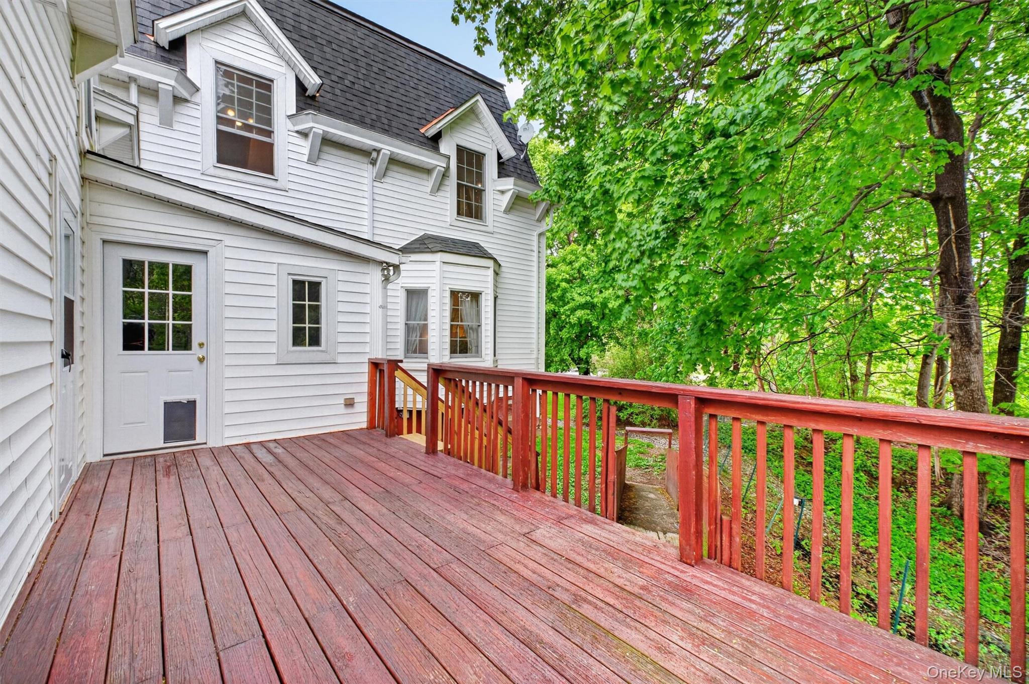 121 Old Glenham Road Fishkill, NY 12524 - Photo 42 of 50 Spacious outdoor deck with wood flooring and matching railings, featuring a verdant tree canopy backdrop and integrated stairs.