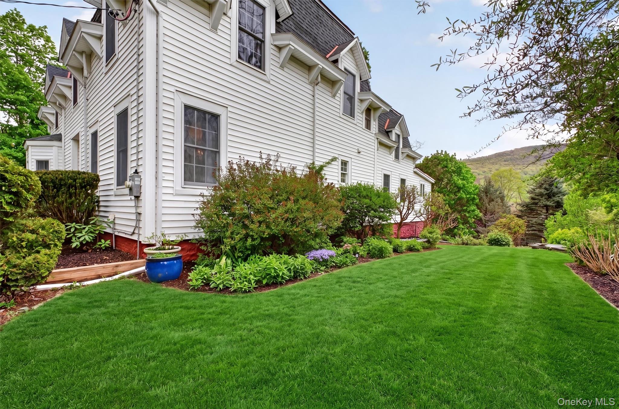 121 Old Glenham Road Fishkill, NY 12524 - Photo 44 of 50 Expansive green lawn framed by manicured hedges, mature trees, and plants, leading to the backyard with views of the hills and mountain.