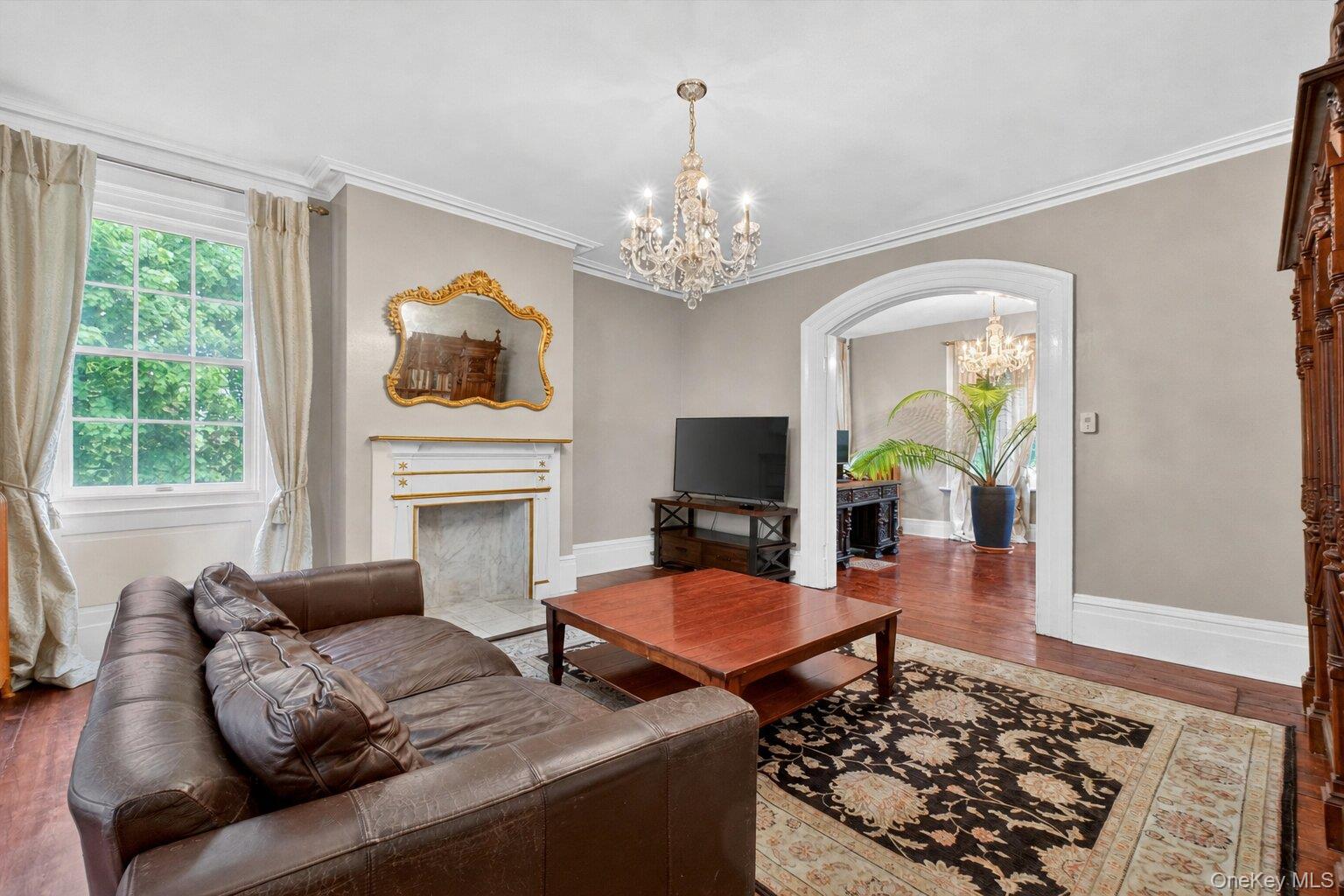 121 Old Glenham Road Fishkill, NY 12524 - Photo 6 of 50 Living area featuring crystal chandelier, hardwood floors, a decorative fireplace with a mantel, an arched doorway leading to another living area, and white trim molding