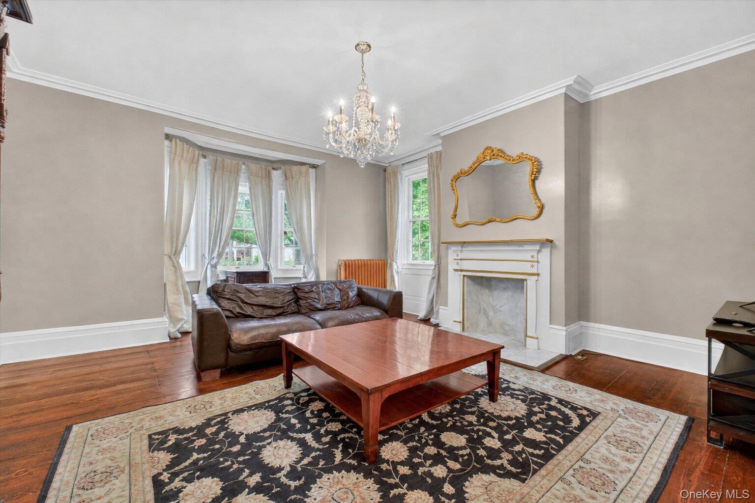 121 Old Glenham Road Fishkill, NY 12524 - Photo 7 of 50 Living area featuring crystal chandelier, hardwood floors, a decorative fireplace with a mantel, bay window looking onto the lawn, and white trim molding