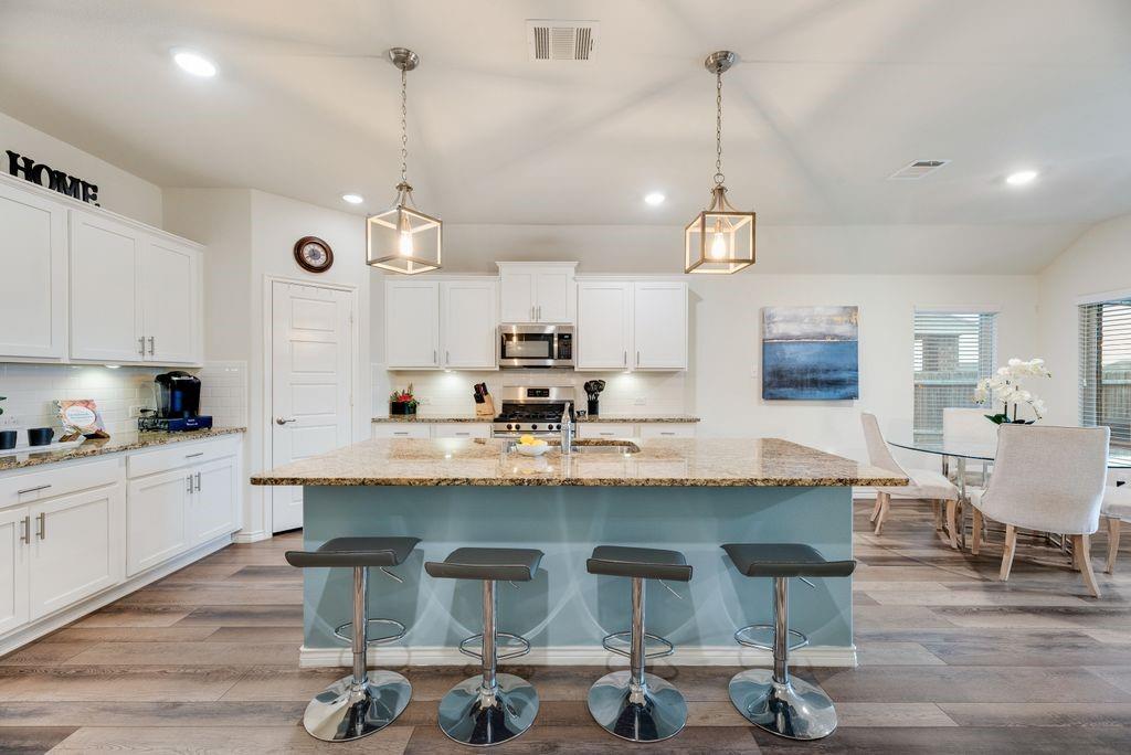 3404 Rio Grande Road Little Elm, TX 75068 - Photo 13 of 39 Spacious kitchen featuring granite countertops, large island with bar seating, gas stove, decorative lighting, and plenty of cabinetry—perfect for cooking and entertaining.