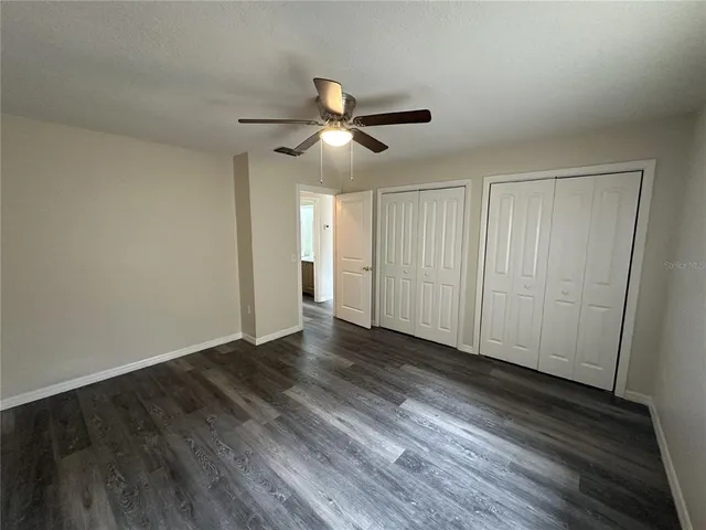 a view of an empty room with wooden floor and a ceiling fan