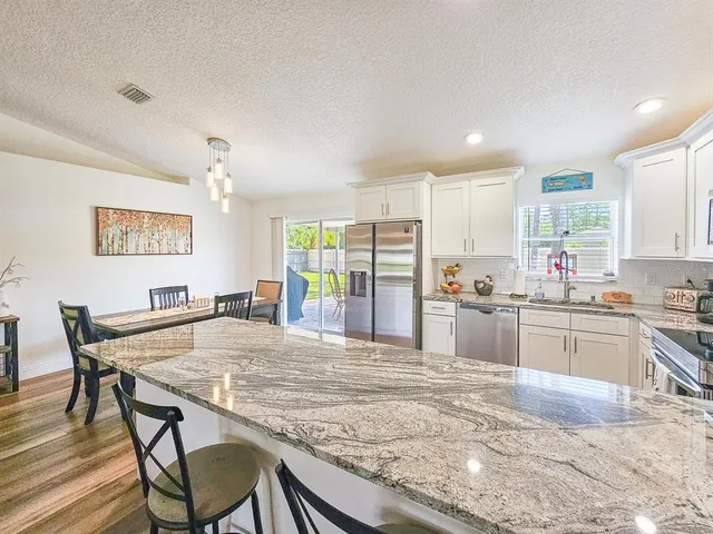 a kitchen with stainless steel appliances granite countertop a stove top oven a sink a dining table and chairs
