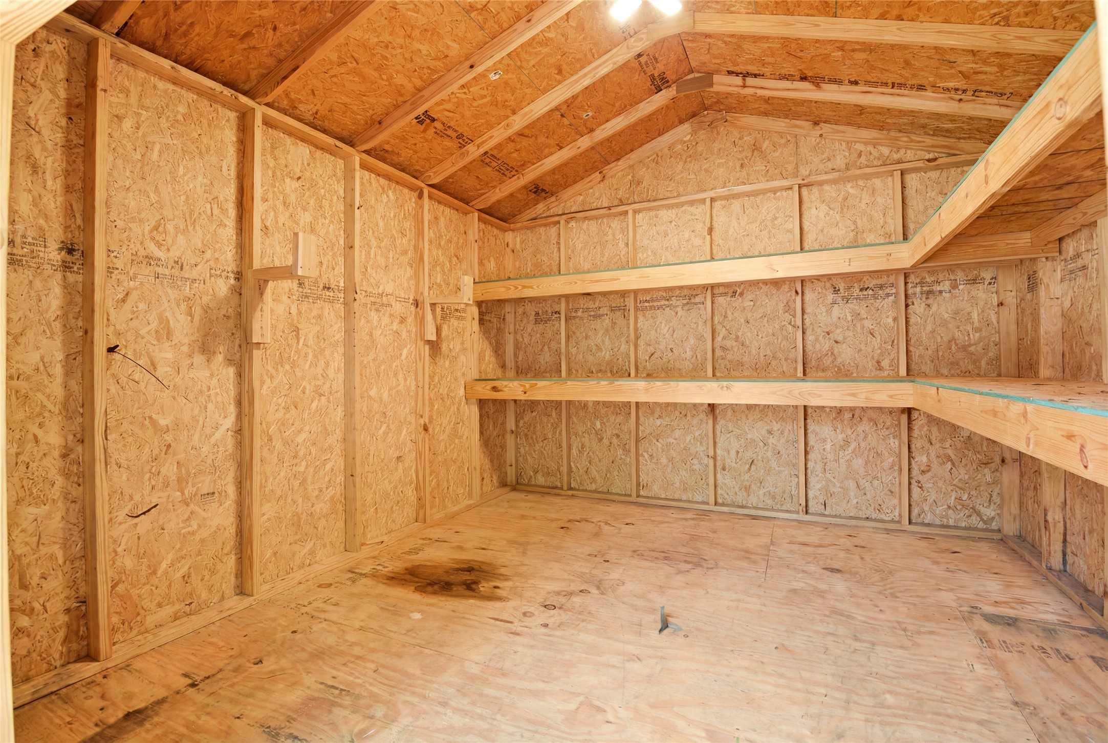 9403 Spaulding Street Houston, TX 77016 - Photo 48 of 50 This photo shows a spacious wooden storage shed with OSB walls and ceiling, featuring sturdy shelving along the walls, perfect for organizing tools or storing items.