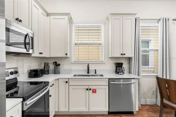 a kitchen with stainless steel appliances white cabinets a sink a stove a window and cabinetry