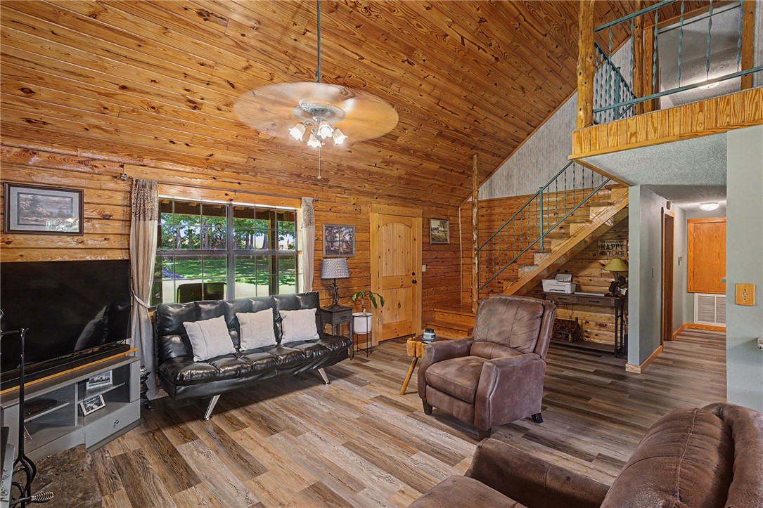 21019 Carter Road West Fork, AR 72774 - Photo 28 of 49 Spacious living area featuring tongue and groove wood paneled walls and vaulted ceilings, wood-finish flooring, a large multi-pane window, and an open staircase with wrought iron railing leading to an upper loft