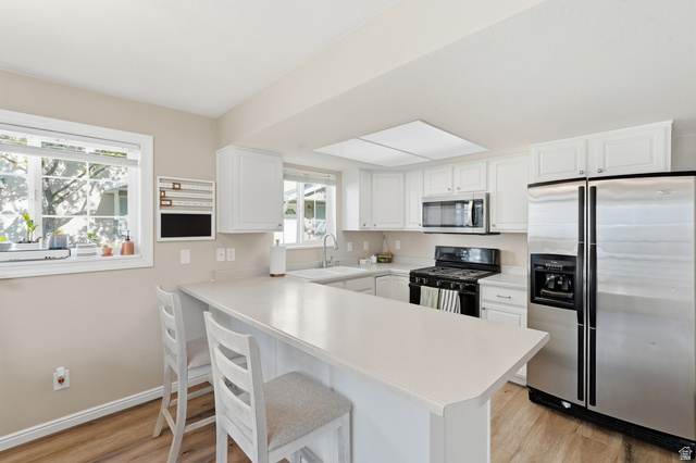 99 Penhurst Place Logan, UT 84341 - Photo 11 of 34 Kitchen featuring white cabinetry, light-toned countertops, wood-finish flooring, stainless steel appliances, and an island with bar seating