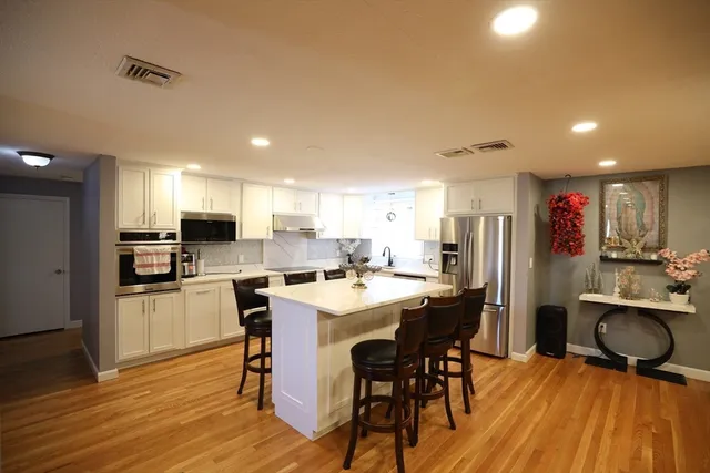 a kitchen with stainless steel appliances kitchen island granite countertop a refrigerator a stove a sink dishwasher and a dining table with wooden floor