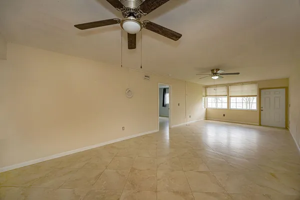 an empty room with ceiling fan and windows