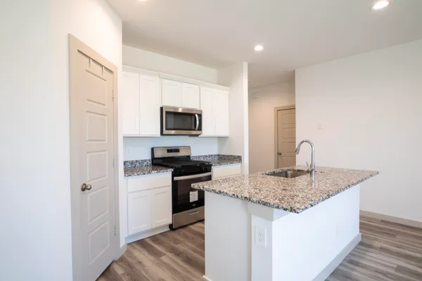 a kitchen with stainless steel appliances granite countertop a sink dishwasher stove and microwave with wooden floor