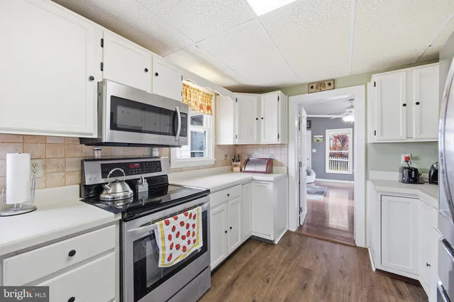 a kitchen with stainless steel appliances a stove a sink a refrigerator white cabinets and wooden floor