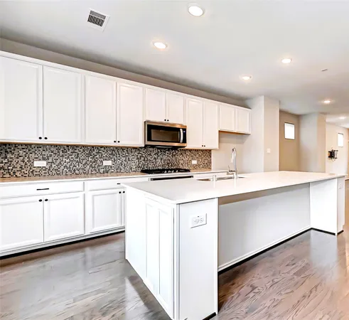 a kitchen with stainless steel appliances granite countertop a stove a sink and white cabinets with wooden floor next to windows