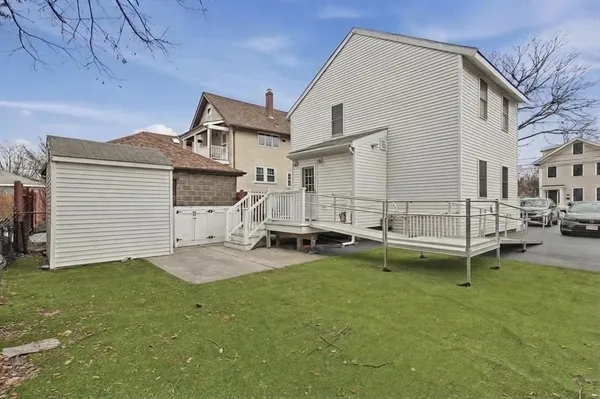 a white house that has a small yard and large trees with wooden fence