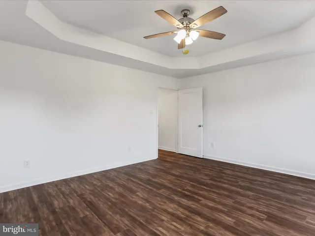a view of an empty room with chandelier fan and wooden floor