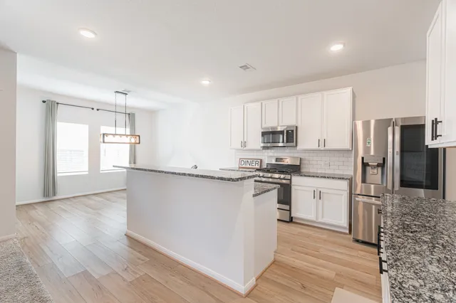 a kitchen with stainless steel appliances granite countertop a refrigerator a stove top oven a sink dishwasher and a dining table with wooden floor