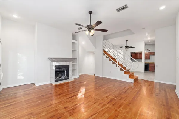 a view of an empty room with wooden floor a ceiling fan and a kitchen