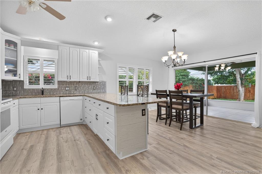 9275 Southeast Mercury Street Hobe Sound, FL 33455 - Photo 24 of 65 a kitchen with stainless steel appliances granite countertop a stove top oven a sink dishwasher a dining table and chairs with wooden floor