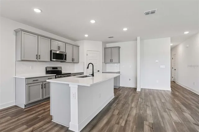 a large white kitchen with stainless steel appliances granite countertop a stove a sink a refrigerator and white cabinets with wooden floor