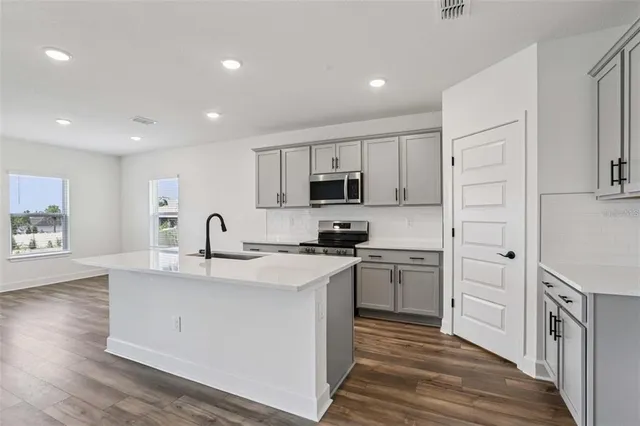 a kitchen with stainless steel appliances granite countertop a sink dishwasher a stove and a refrigerator with wooden floor