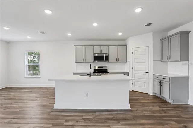 a kitchen with stainless steel appliances granite countertop a stove a sink a refrigerator white cabinets and wooden floor