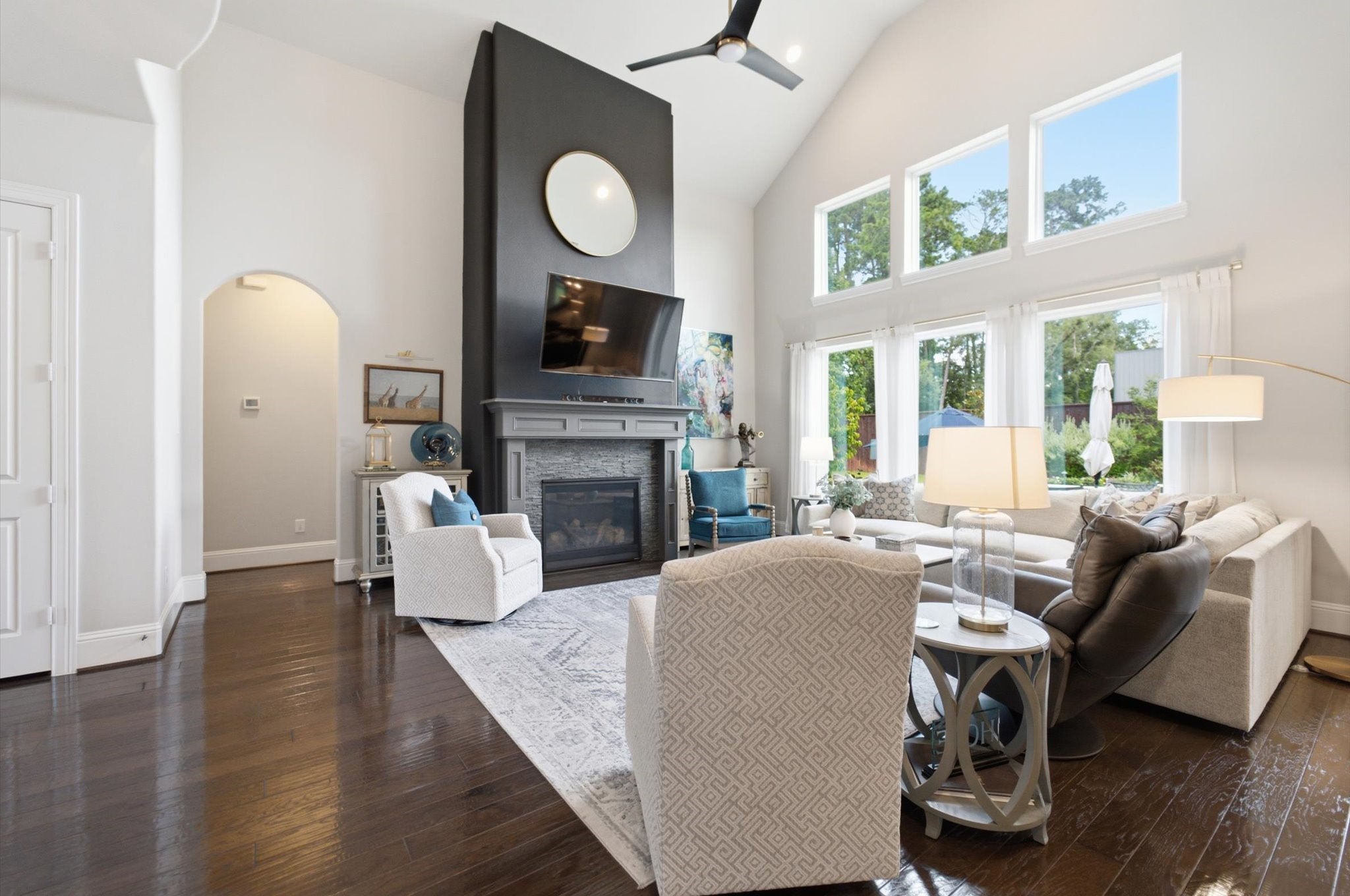 23722 Thortons Park Lane Spring, TX 77389 - Photo 29 of 48 This spacious living room features high ceilings and large windows, allowing abundant natural light. It includes a modern fireplace, sleek dark flooring, and a stylish seating area, creating an inviting and elegant atmosphere.
