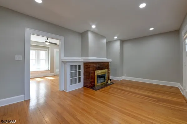 a view of an empty room with wooden floor fireplace and a window