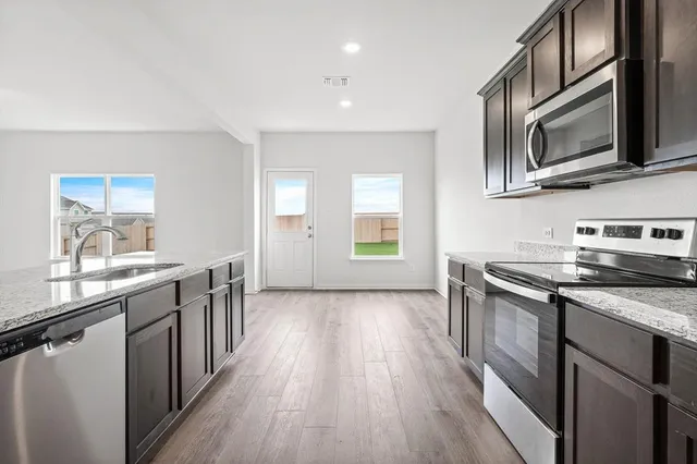 a kitchen with stainless steel appliances granite countertop a stove top oven a sink dishwasher a microwave oven and a refrigerator with wooden floor