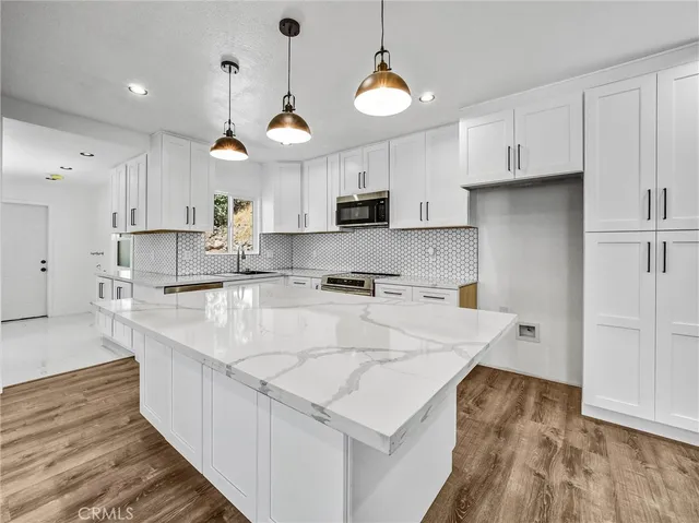 a large white kitchen with kitchen island a stove a sink a refrigerator and white cabinets with wooden floor