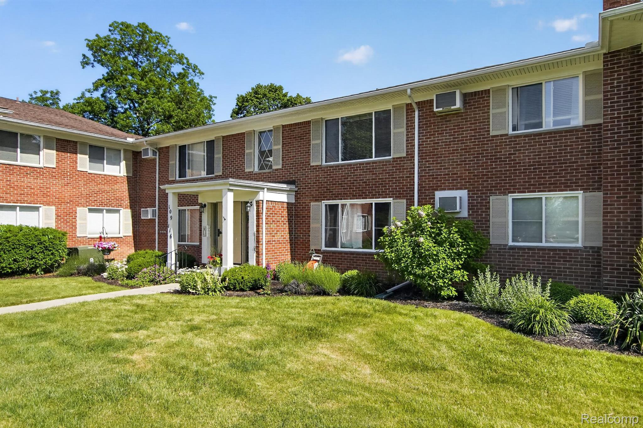 24111 Meridian Road, Unit 116 Grosse Ile, MI 48138 - Photo 4 of 26 Brick exterior with multiple windows featuring louvered shutters, a covered entry with columns, and a landscaped front garden with a manicured lawn