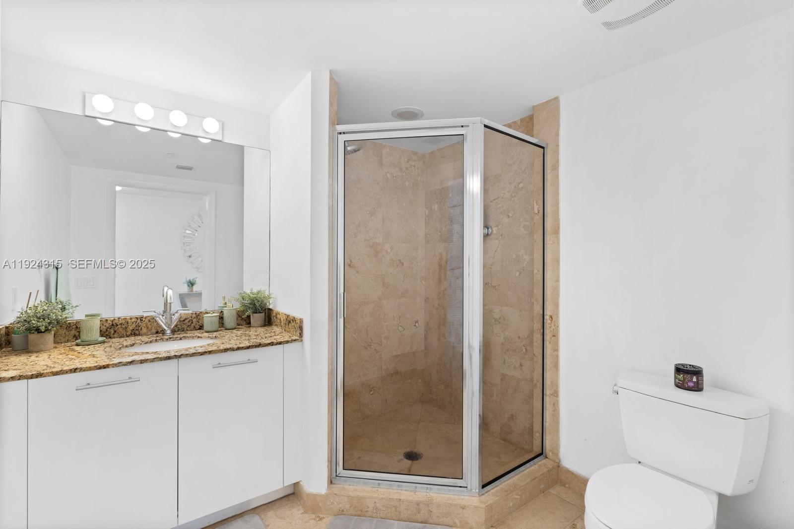 41 Southeast 5th Street, Unit 510 Miami, FL 33131 - Photo 15 of 38 a bathroom with a granite countertop sink a toilet a mirror and shower