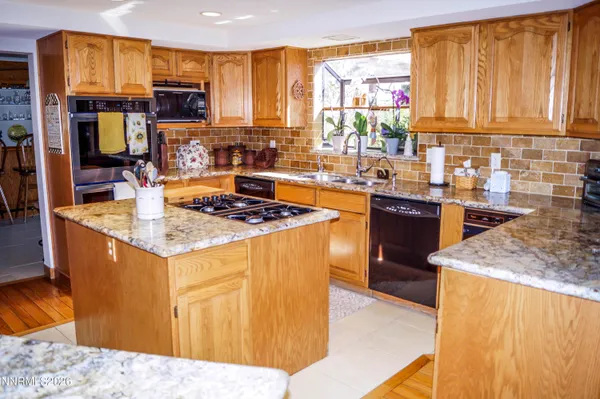 a kitchen with stainless steel appliances granite countertop a stove top oven a sink dishwasher and wooden cabinets with large windows