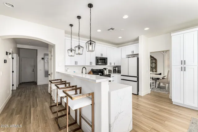 a kitchen with stainless steel appliances kitchen island granite countertop a refrigerator a stove a microwave oven a sink with island and chairs with wooden floor