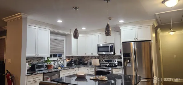 a kitchen with stainless steel appliances granite countertop a refrigerator a stove a sink and white cabinets with wooden floor