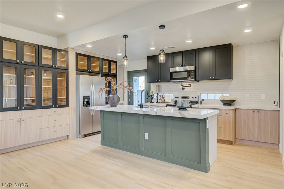 732 8th Street Boulder City, NV 89005 - Photo 4 of 15 Dual tone kitchen featuring dual tone cabinetry, stainless steel appliances, decorative light fixtures, a kitchen island with sink, and light wood finished floors