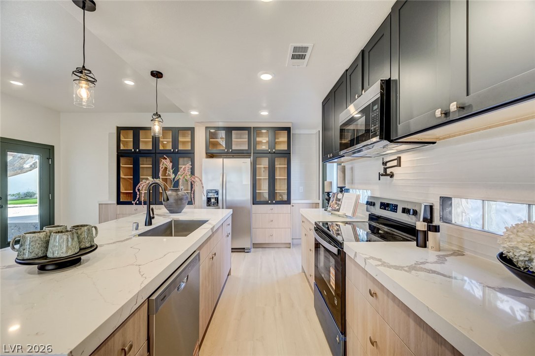 732 8th Street Boulder City, NV 89005 - Photo 6 of 15 Kitchen with healthy amount of natural light, stainless steel appliances, two tone cabinetry, decorative light fixtures, and light stone counters