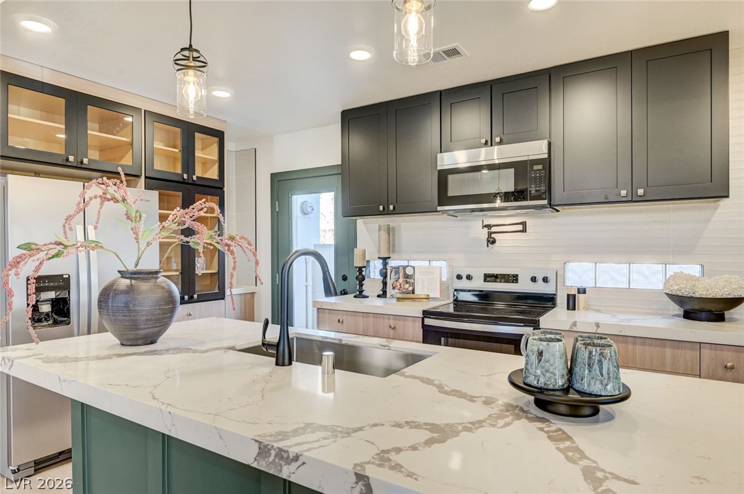 732 8th Street Boulder City, NV 89005 - Photo 7 of 15 Two tone kitchen with stainless steel appliances, light stone countertops, pendant lighting, glass fronted cabinets, and dual tone cabinetry