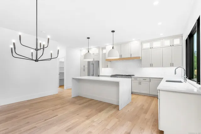 a kitchen with stainless steel appliances granite countertop a sink a stove a refrigerator and white cabinets with wooden floor