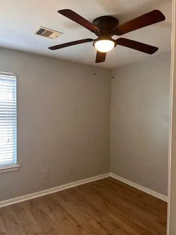 an empty room with wooden floor chandelier fan and windows