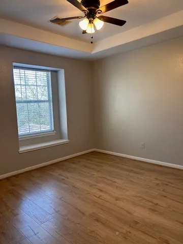an empty room with wooden floor fan and windows