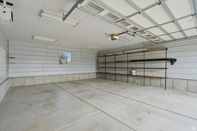791 East Saddle Road Grantsville, UT 84029 - Photo 44 of 46 Spacious garage featuring a concrete floor, corrugated metal walls, built-in shelving, overhead lighting, and a window