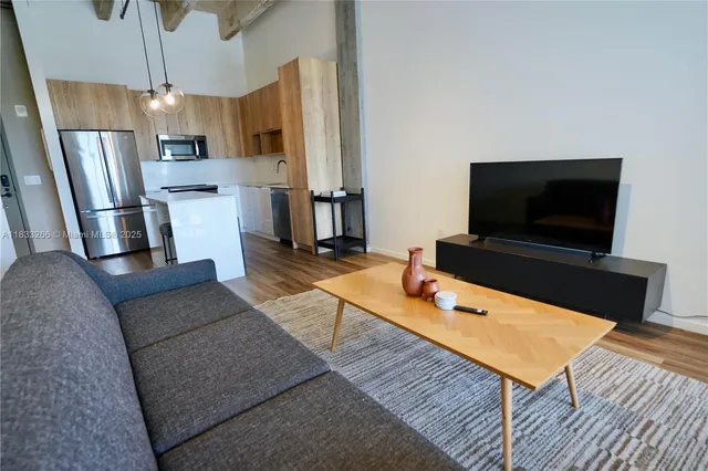 a living room with stainless steel appliances furniture a flat screen tv and kitchen view