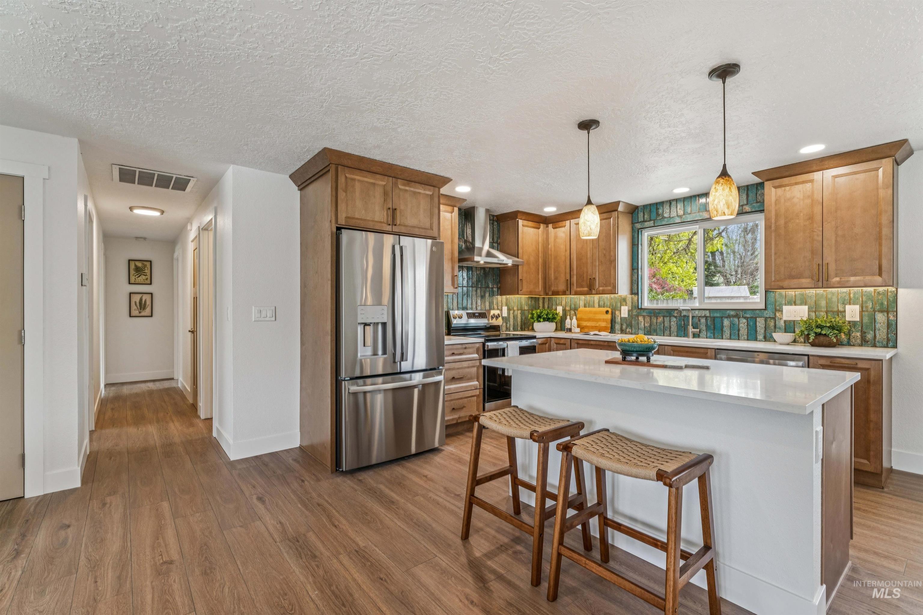 9709 West McMillan Road Boise, ID 83704 - Photo 12 of 50 Kitchen featuring stainless steel appliances, a kitchen breakfast bar, wood finish cabinets, a center island, and decorative light fixtures