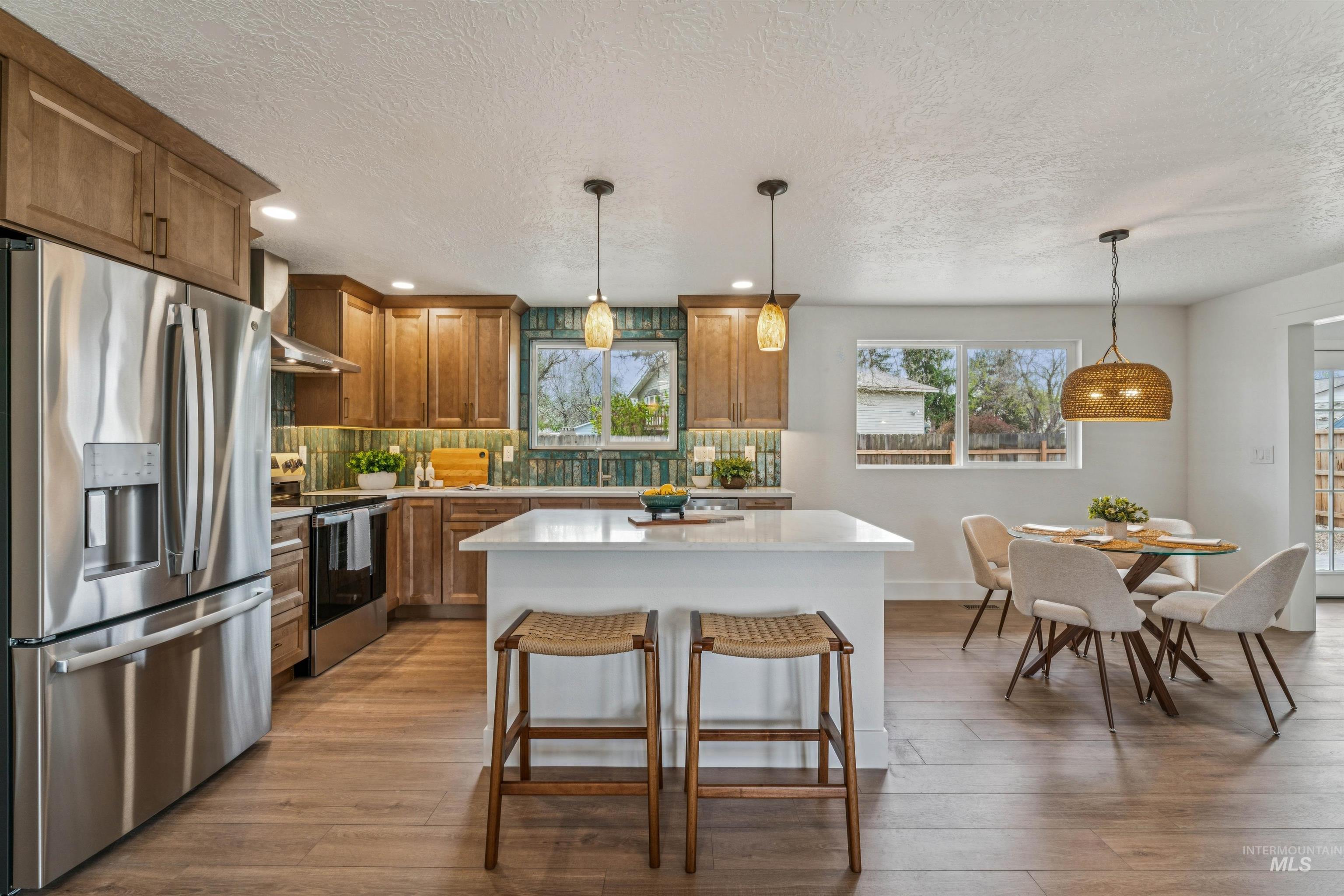 9709 West McMillan Road Boise, ID 83704 - Photo 13 of 50 Kitchen with stainless steel appliances, wood finish cabinets, a kitchen island, decorative light fixtures, and a textured ceiling