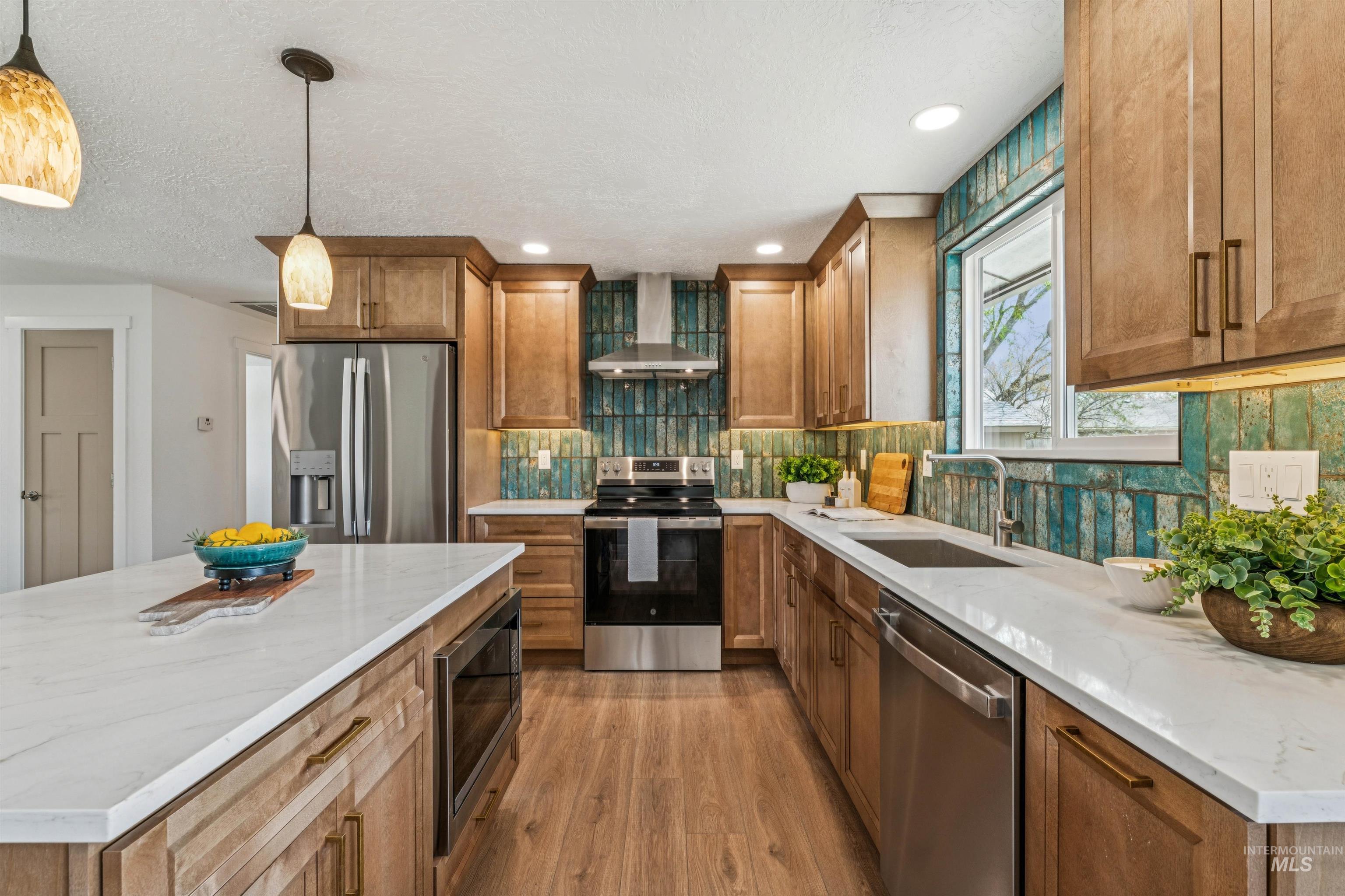 9709 West McMillan Road Boise, ID 83704 - Photo 16 of 50 Kitchen featuring stainless steel appliances, extractor fan, wood finish cabinets, light wood-style floors, and light stone countertops
